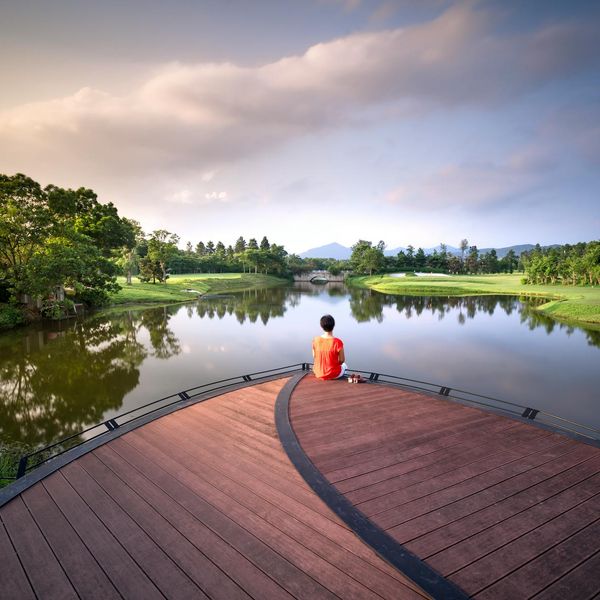 Person meditating peacefully by a calm lake at sunrise.